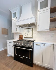 white kitchen with wall clock above range featuring a white Hoodsly Curved wood range hood with ventilation