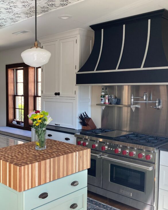 white, light green, and black kitchen with butcher block island end featuring a large, black Hoodsly Curved hood with stainless steel strapping and flat trim