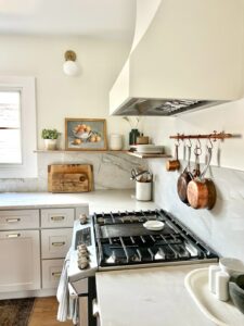 rustic kitchen with plants and artwork featuring a white Hoodsly Sloped without Trim wooden range hood