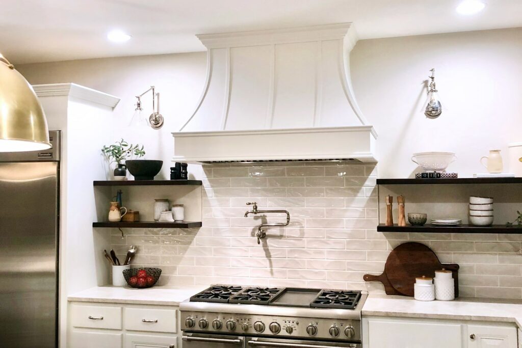 white kitchen with mixed metallics featuring black floating shelves and a white Hoodsly curved hood with strapping and classic trim